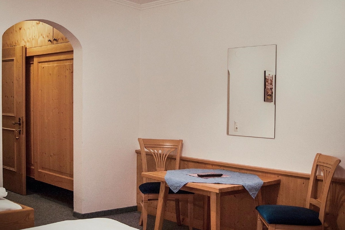 A room with a wooden door, a mirror, a small table with chairs, and a bed.