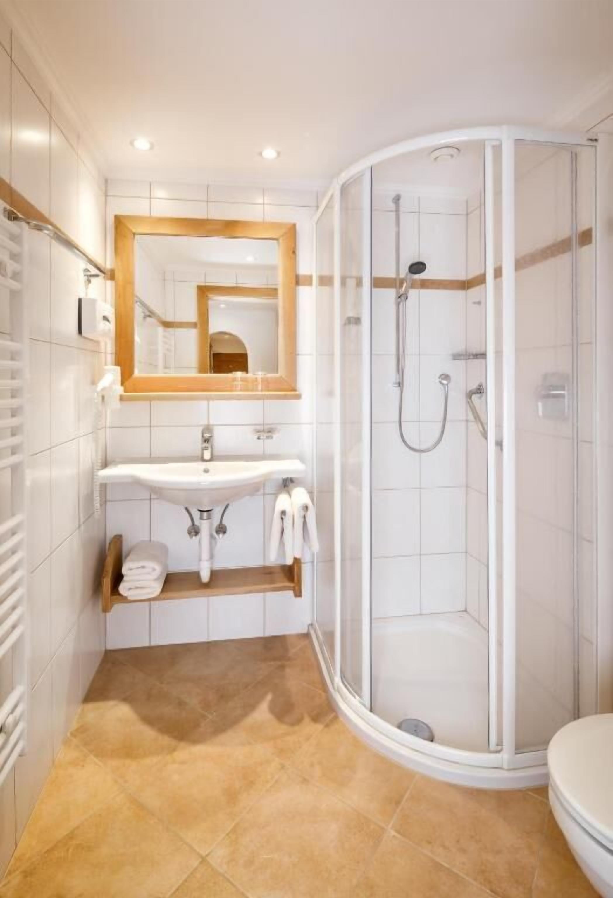 Un baño moderno con lavamanos, espejo y ducha blancos.