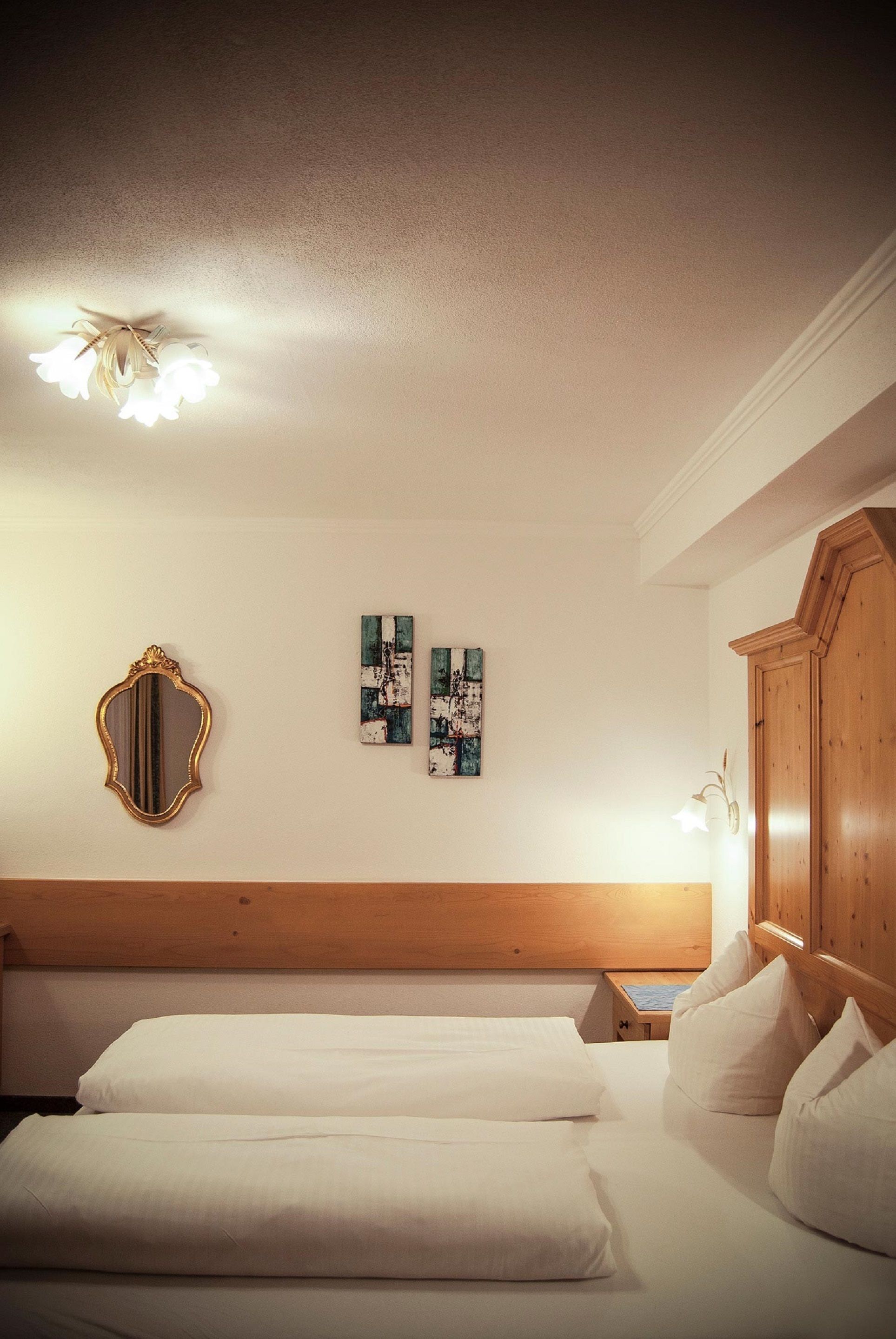 Hotellihuone, jossa on puinen sängynpääty, kaksi valkoisilla lakanoiden peittämää sänkyä, peili ja kaksi abstraktia maalausta seinällä.