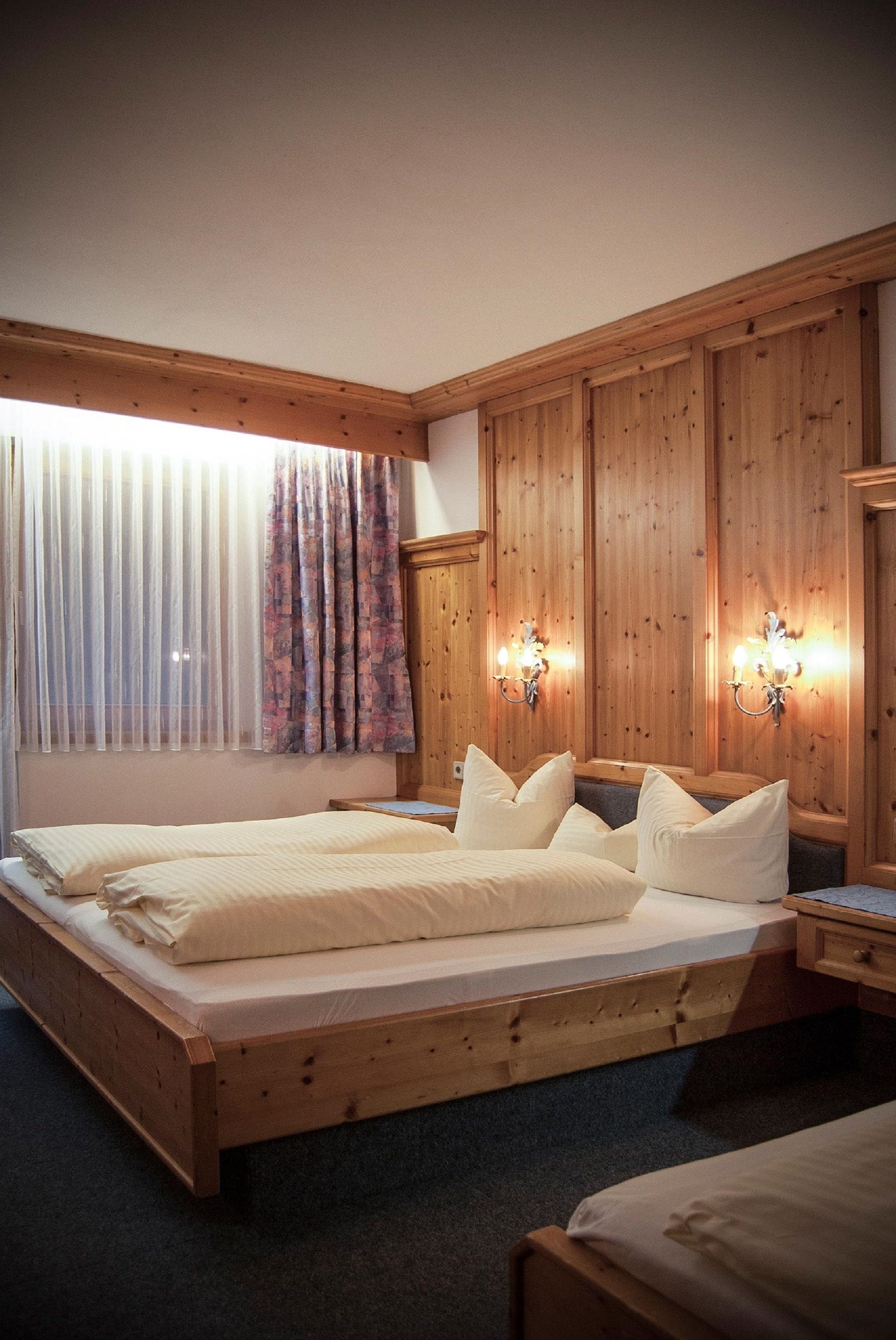 Ein Zimmer aus Holz mit einem großen Bett, zwei Wandleuchten und einem Fenster mit durchsichtigen Vorhängen.