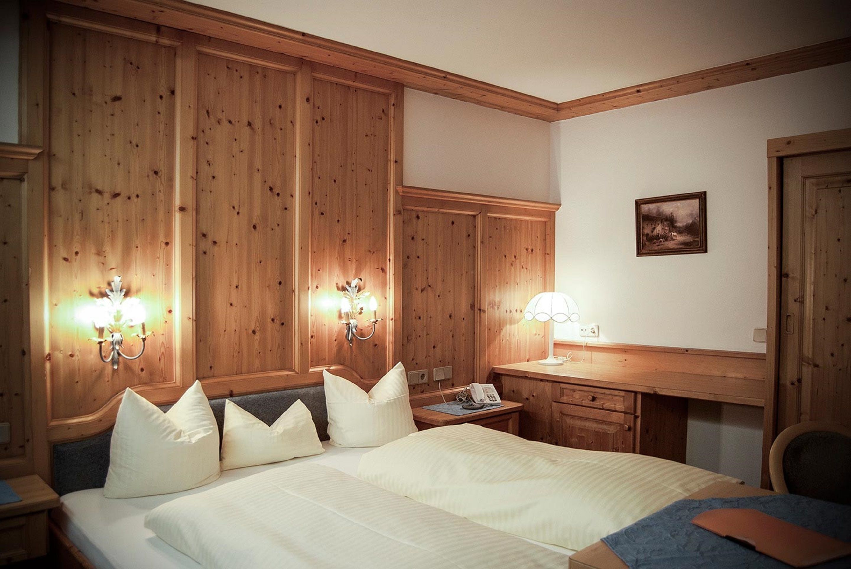 Een hotelkamer met een groot bed, houten lambrisering aan de wanden, een bureau met een lamp en een klein nachtkastje.