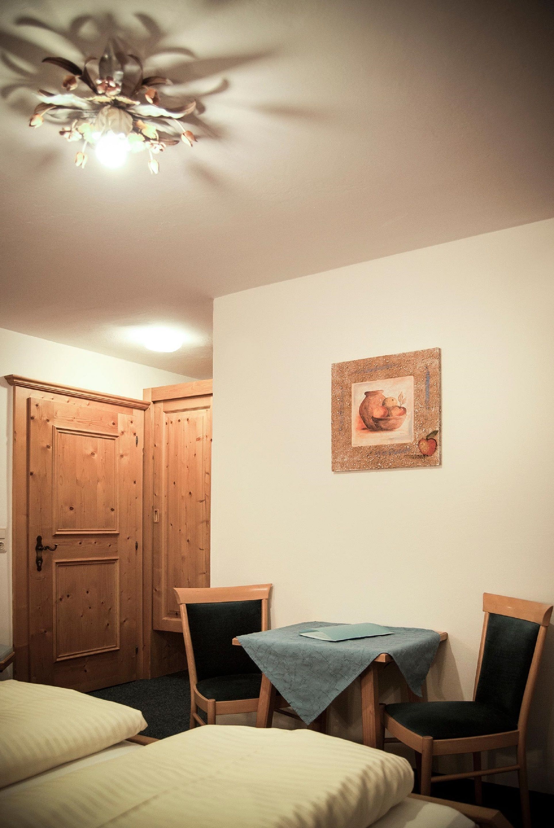 Ein Zimmer mit zwei Betten, einer Holztür, einem Tisch mit Tischdecke und einem gerahmten Bild an der Wand.