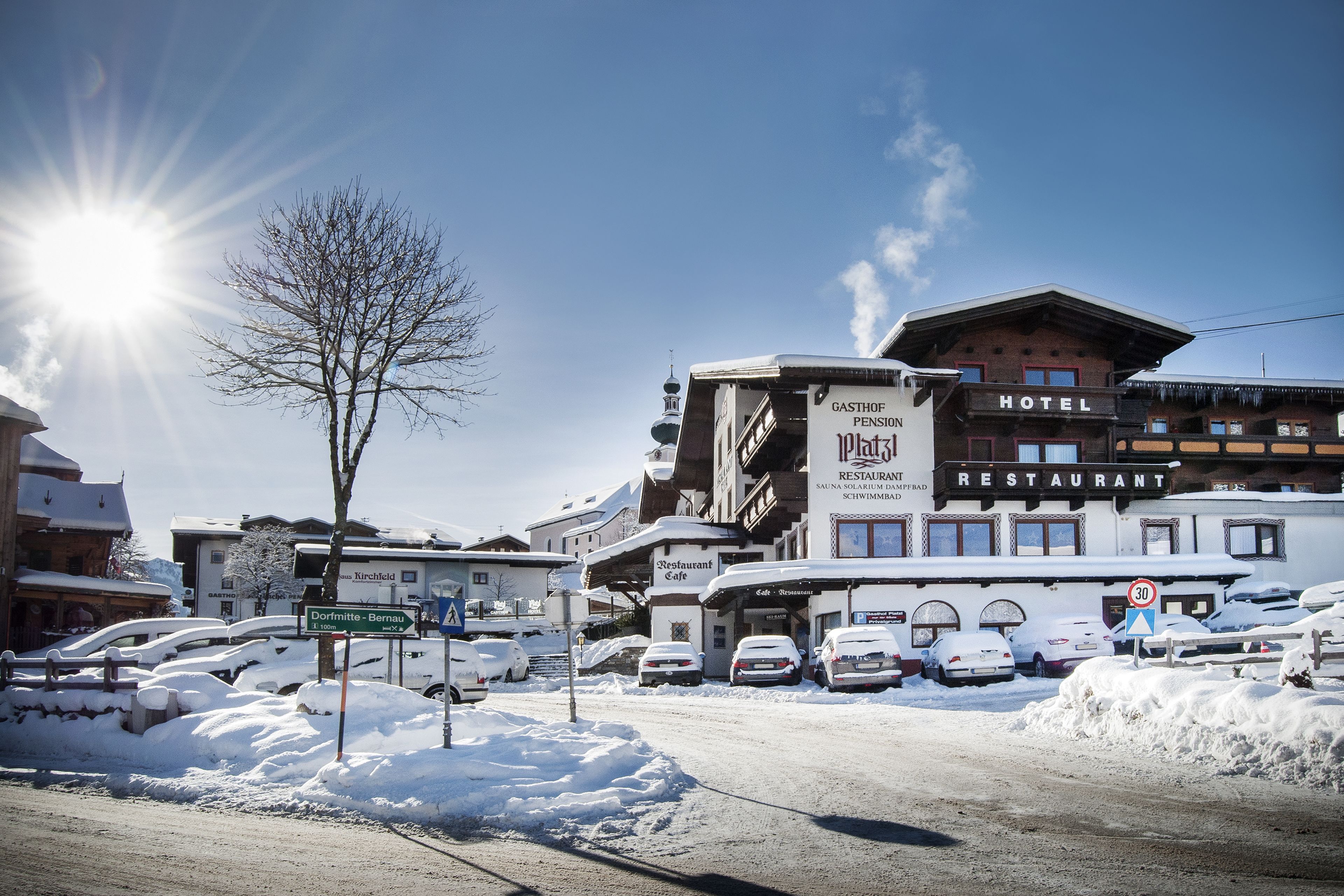 Un hotel con restaurante y una pensión en la planta baja, rodeado de coches cubiertos de nieve y un cielo despejado.