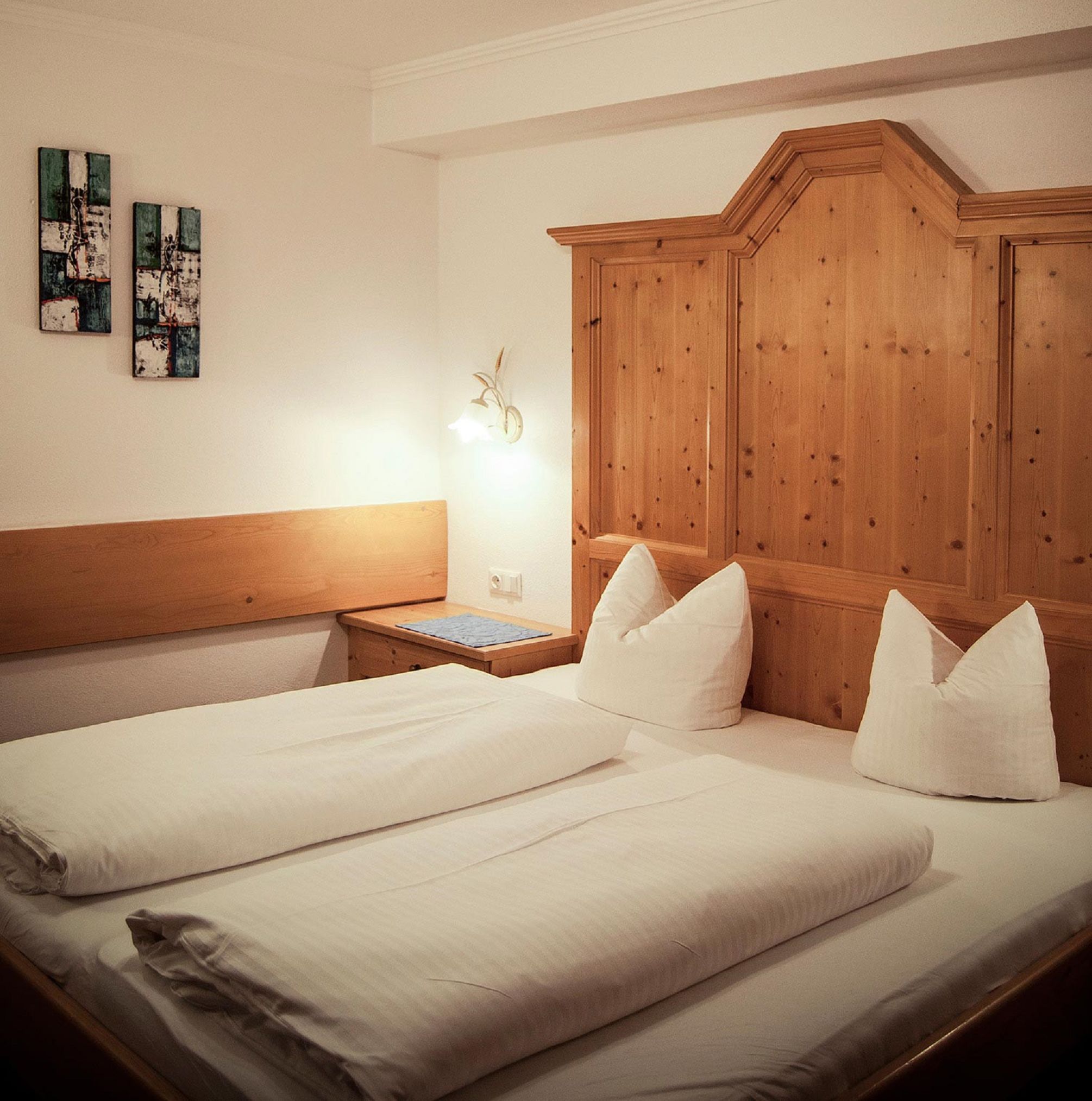 Ein Hotelzimmer mit einem Holzkopfteil, einem Bett mit weißen Leinentüchern und zwei an der Wand befestigten Bildern.