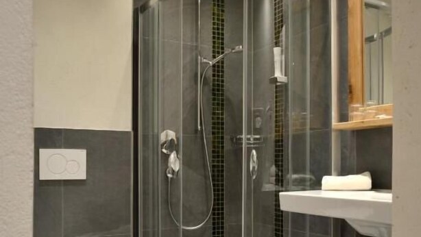 A modern bathroom with a glass-enclosed shower, a toilet, and a sink with a mirror. - Hotel Platzl (Wildschönau)