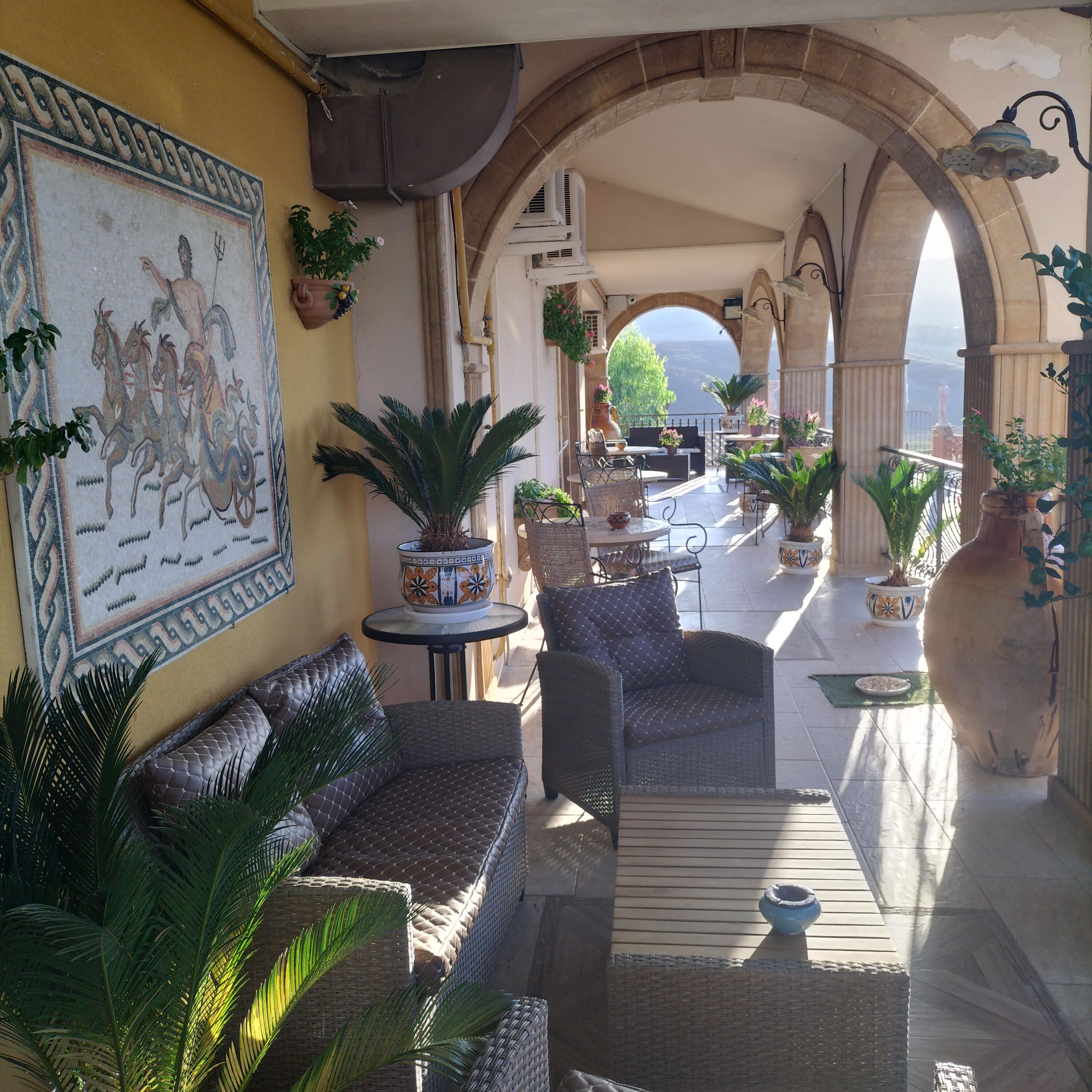 An outdoor seating area with wicker furniture, potted plants, and a mural on the wall.
