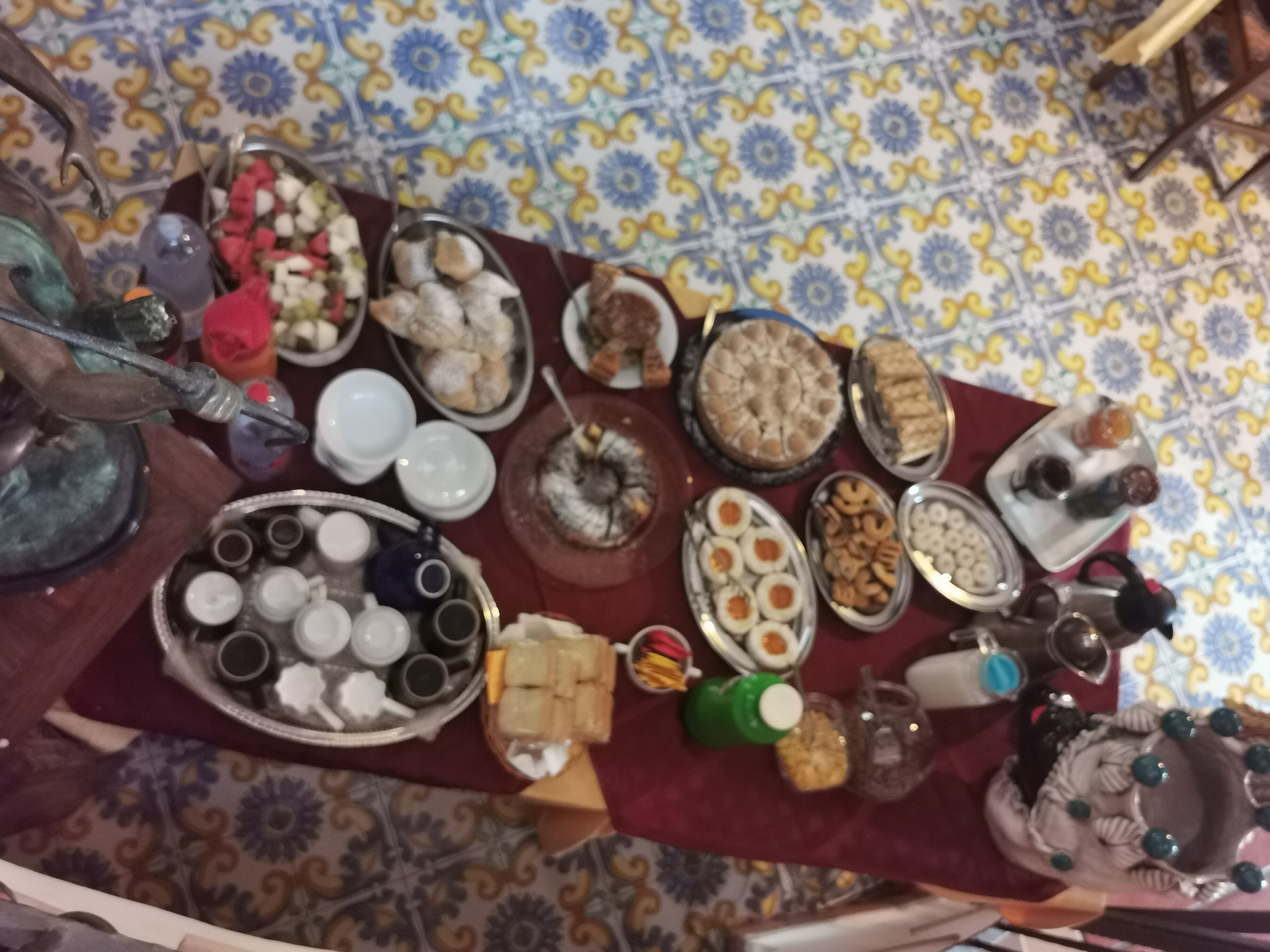 Ein Tisch mit verschiedenen Speisen und Besteck, darunter Teller, Schüsseln und Tassen, auf einer Tischdecke mit Muster.