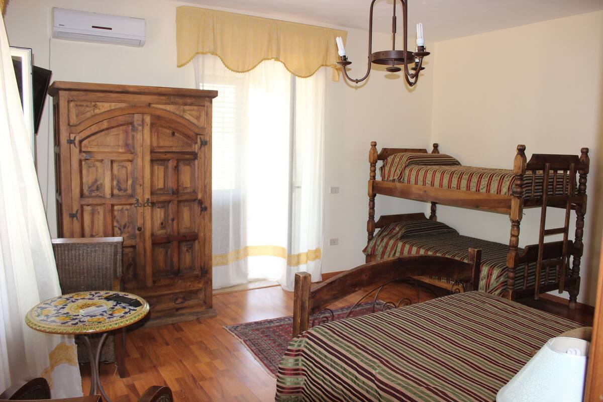 Una habitación con un armario de madera, una cama con colcha a rayas, una mesita redonda y una araña.