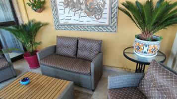 A wicker sofa with patterned cushions, a wooden coffee table, and a potted plant on a tiled floor.