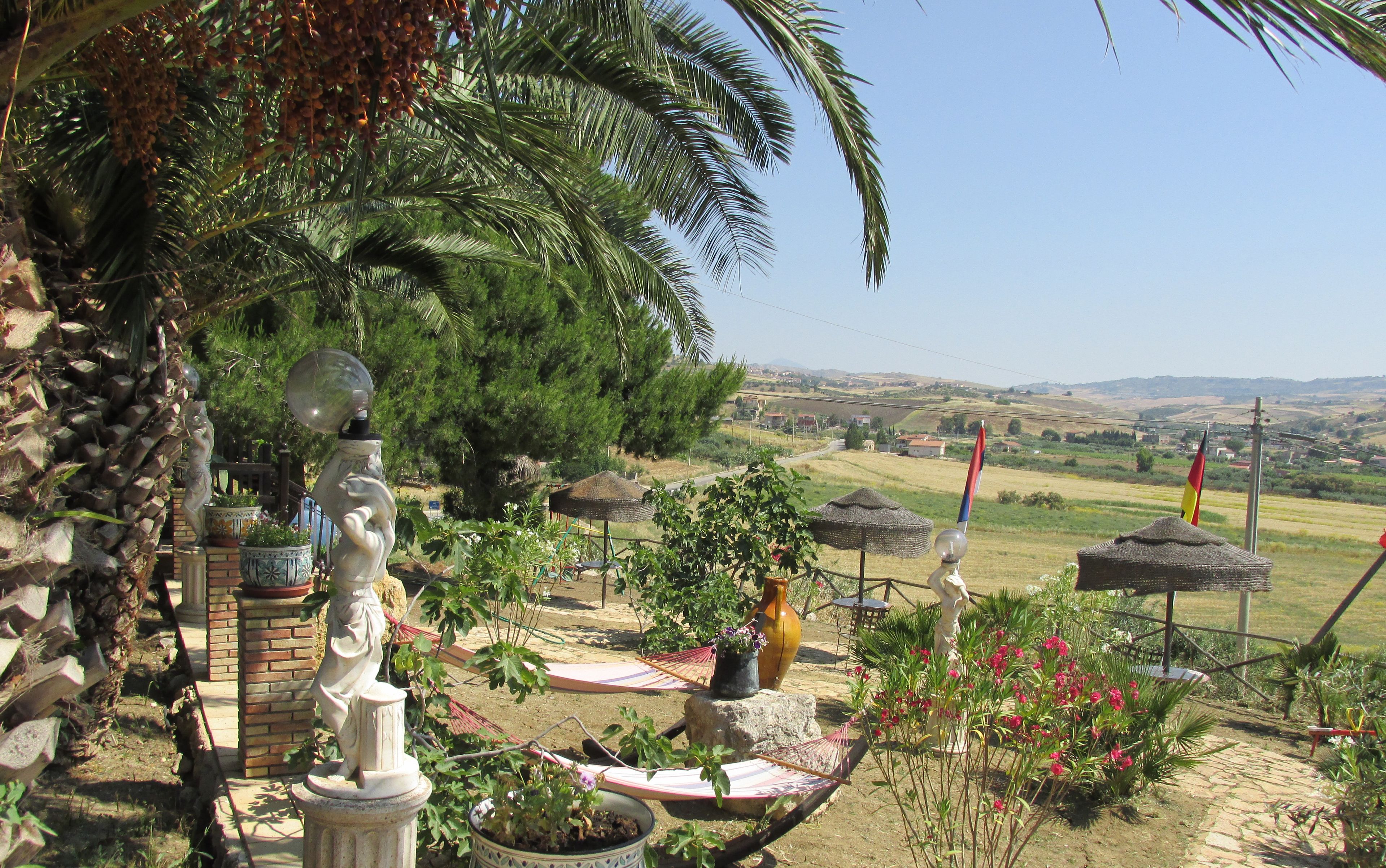 A garden with a statue, a palm tree, and a view of the countryside.