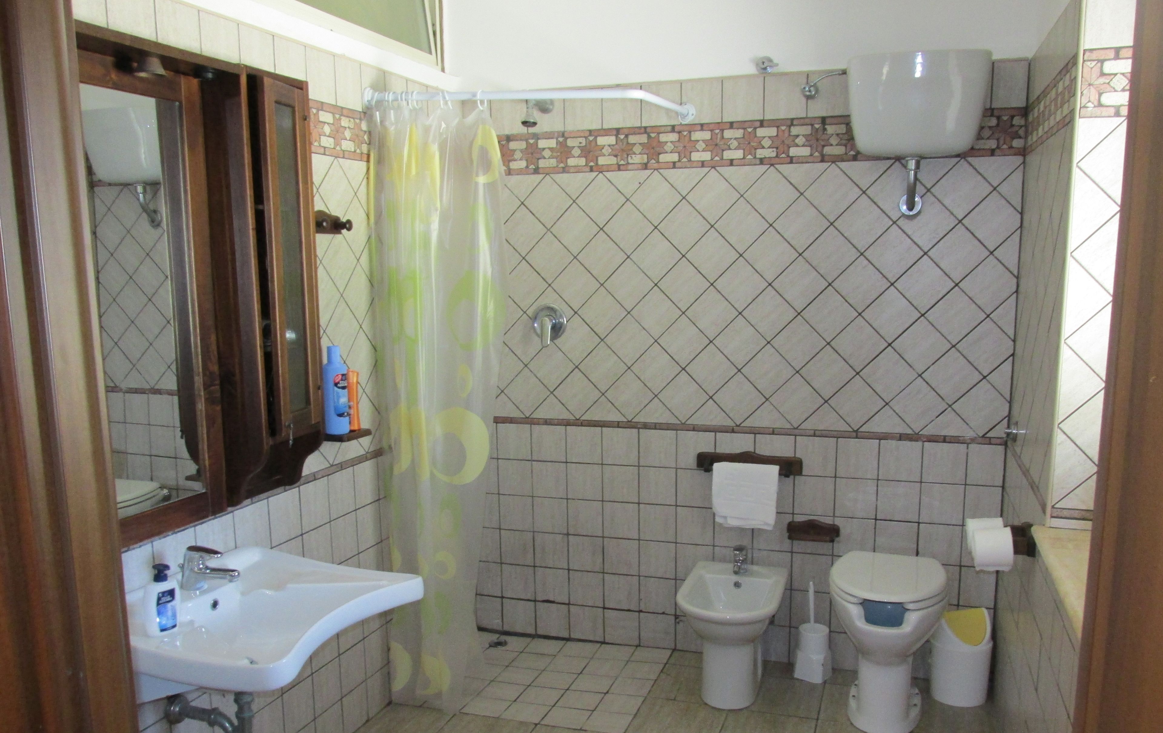 Un bagno con lavandino, due servizi igienici, una tenda da doccia e uno specchio.