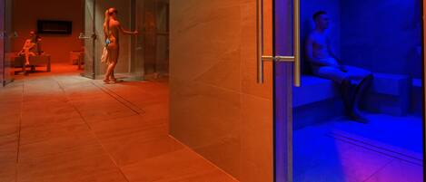 A modern spa area with a glass partition, a man sitting on a bench, and a woman standing by the entrance.