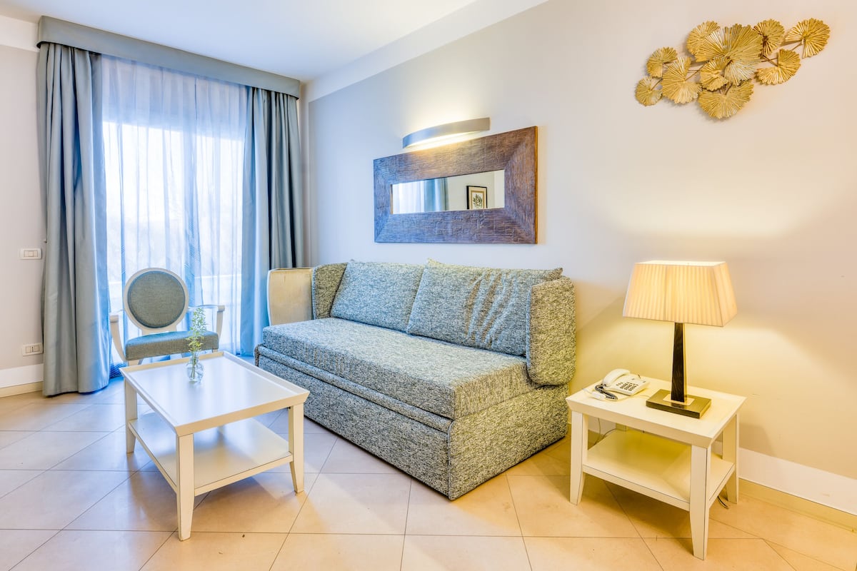 A modern living room with a sofa, a small table, a lamp, and a decorative wall piece.