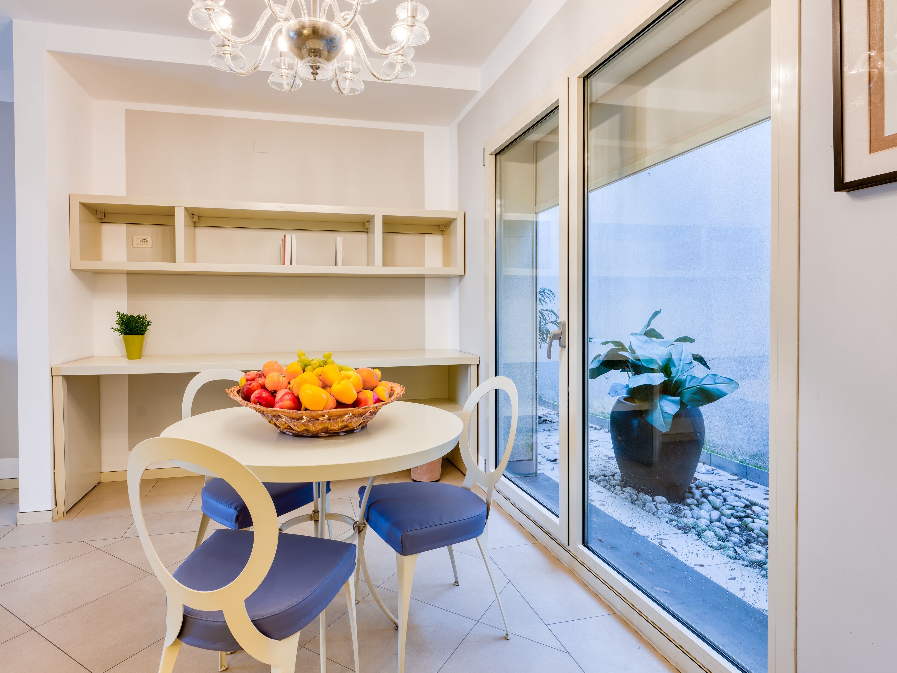 Una cocina moderna con una mesa de comedor, sillas, un frutero y un amplio ventanal con vistas al exterior.