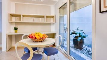 Una cocina moderna con una mesa de comedor, sillas, un frutero y un amplio ventanal con vistas al exterior.