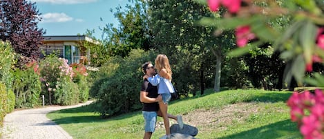 Un couple s’embrasse dans un jardin, avec un chemin pavé, de la verdure et un bâtiment en arrière-plan.