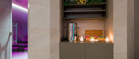 Un baño moderno con un estante empotrado que contiene una cafetera, velas y plantas decorativas.