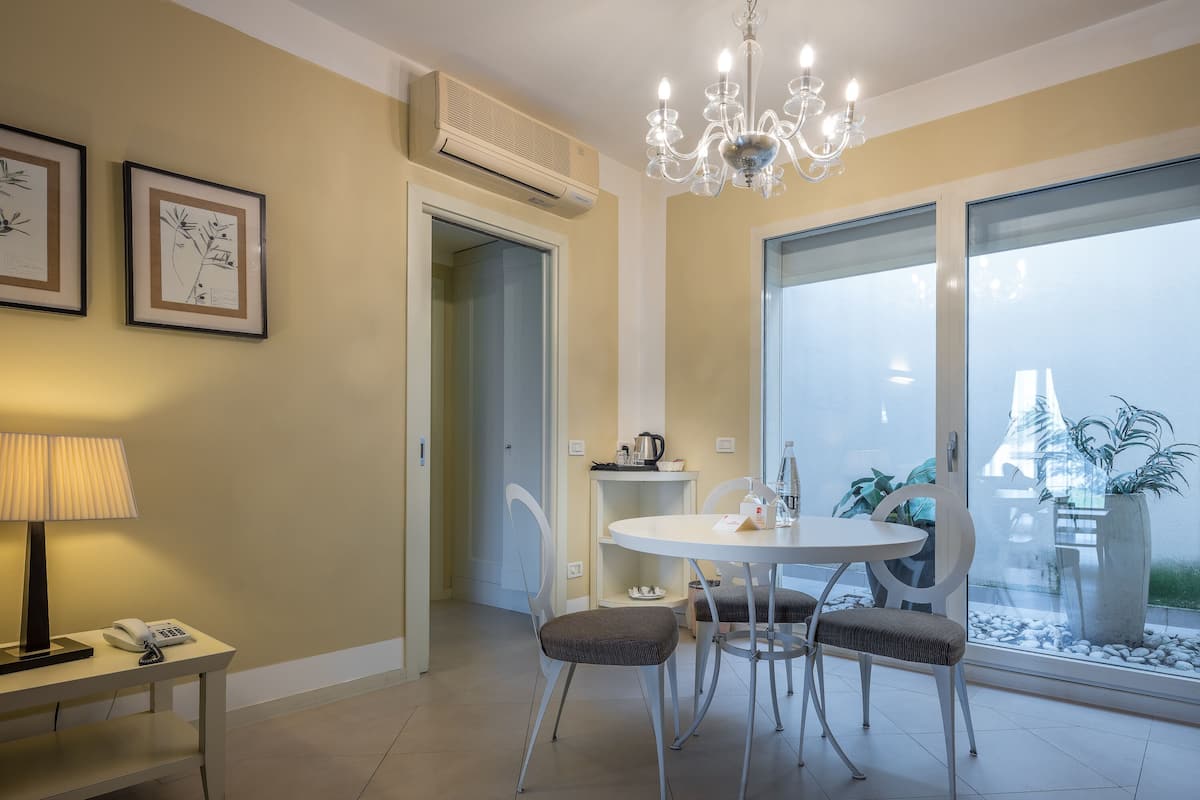 A dining area with a round table, two chairs, a chandelier, a wall-mounted air conditioner, and framed artwork.
