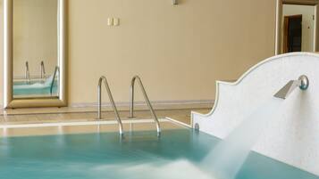 A swimming pool with metal ladders, a tiled floor, and a wall-mounted mirror.