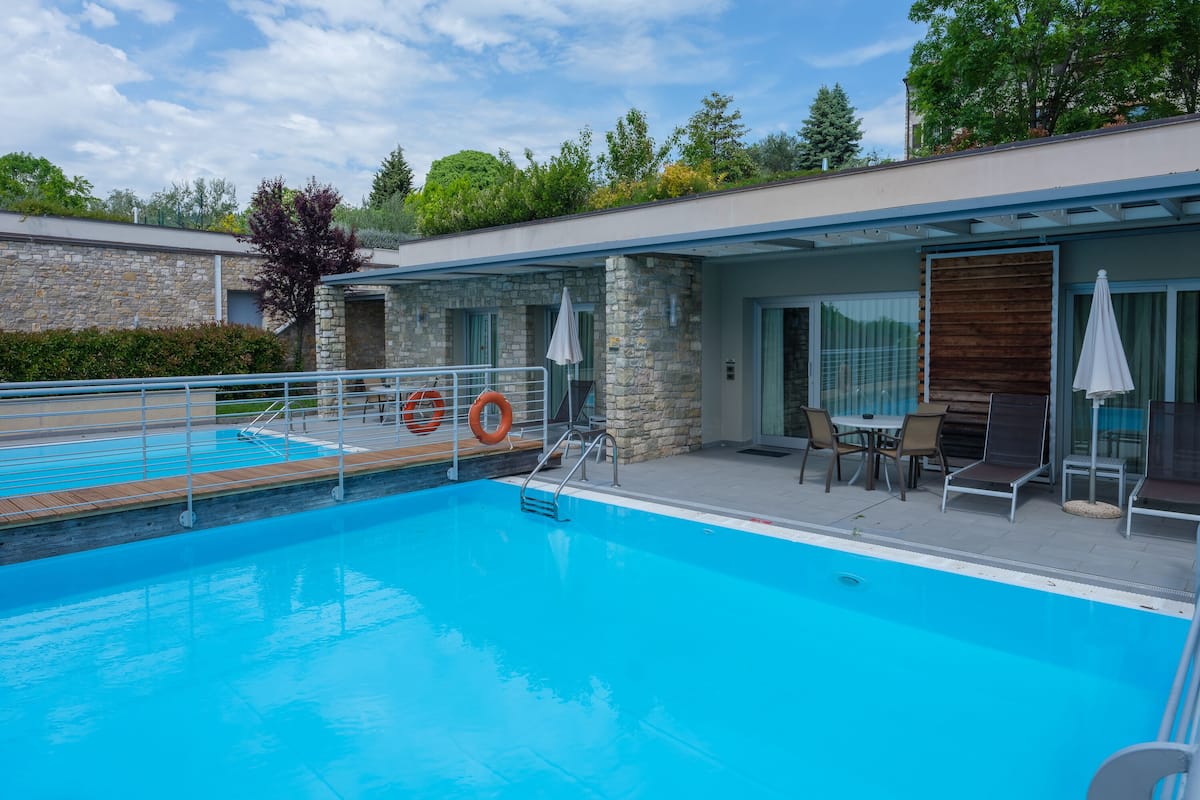 A swimming pool with a stone wall and a covered patio area with outdoor seating.