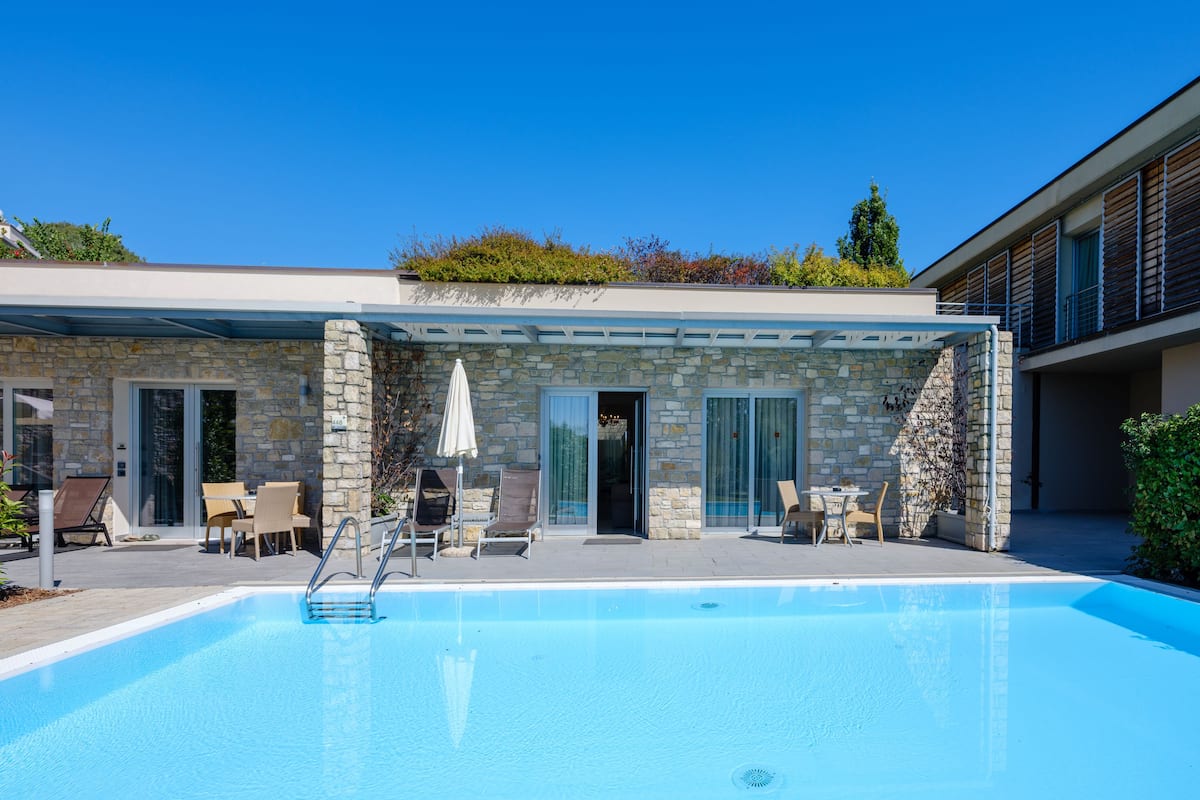 A modern outdoor pool area with stone walls, lounge chairs, and a covered patio.