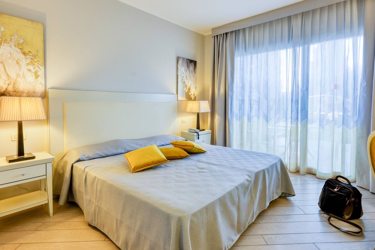 A hotel room with a bed, bedside lamps, a nightstand, a desk, and a chair.