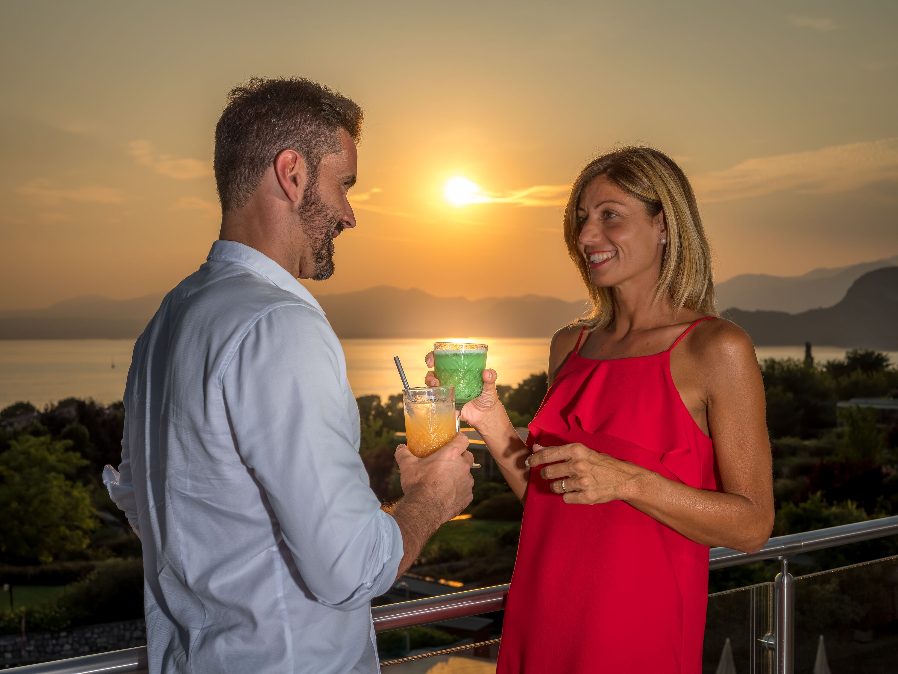 Ein Paar hält Getränke auf einem Balkon mit Blick auf einen Sonnenuntergang.