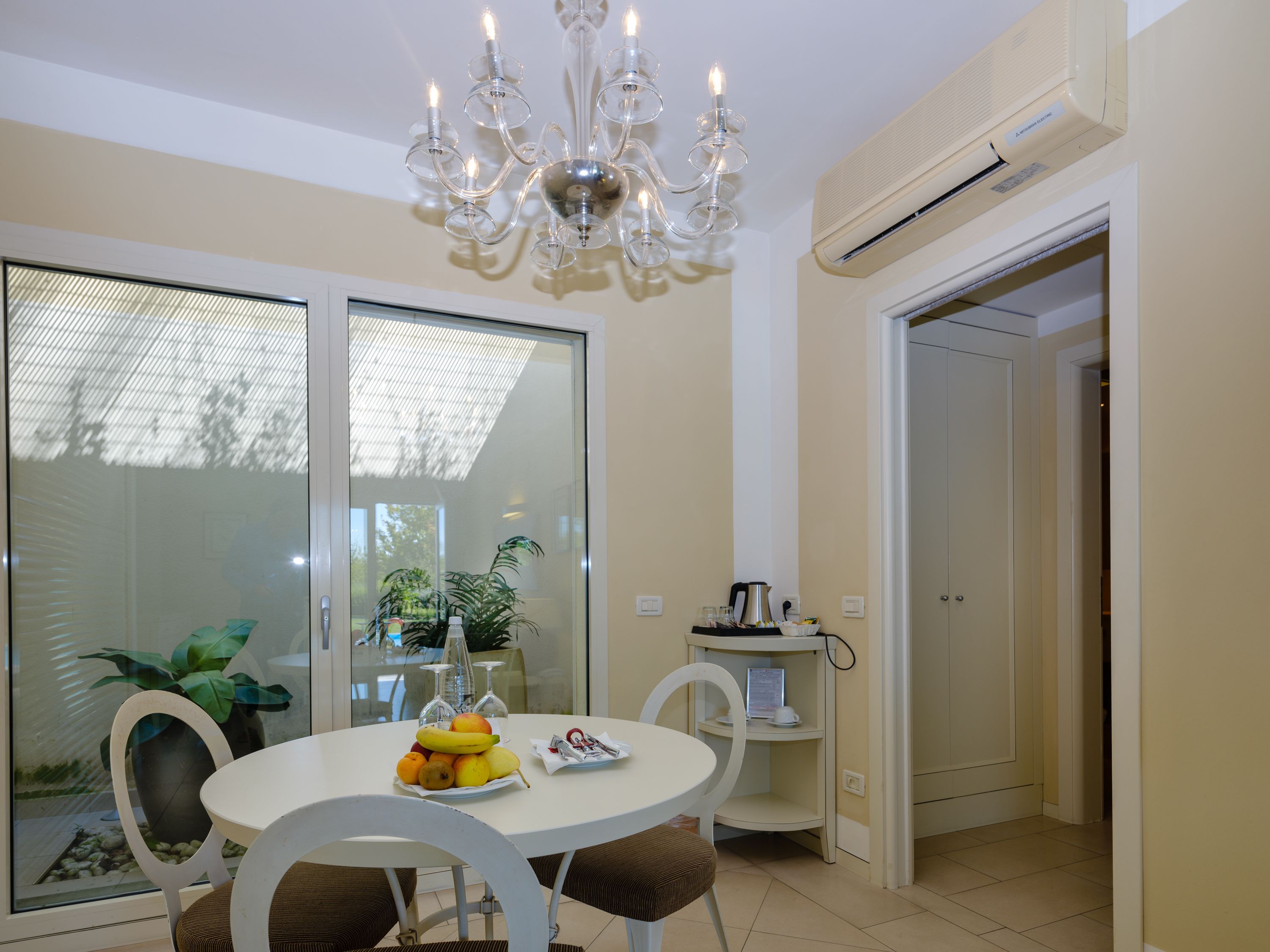 A dining area with a round table, chairs, a chandelier, and a glass partition.