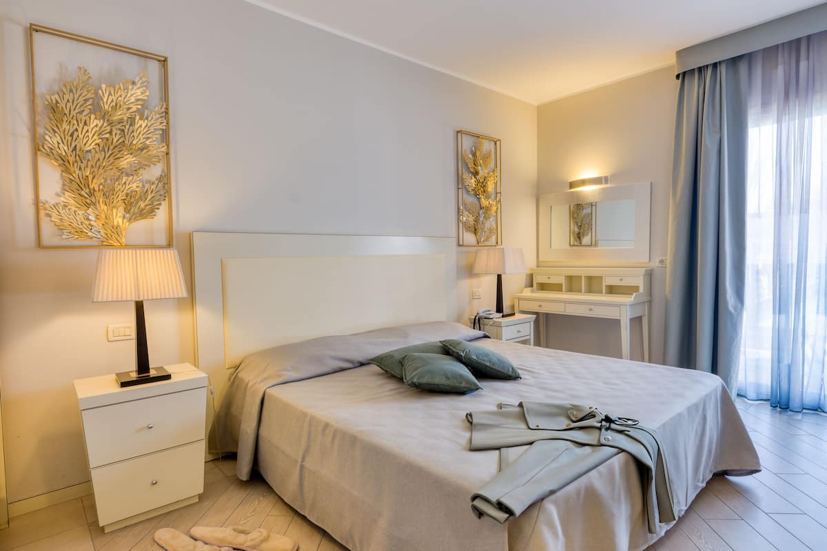 A neatly arranged bedroom with a bed, bedside tables, a vanity, and artwork on the walls.