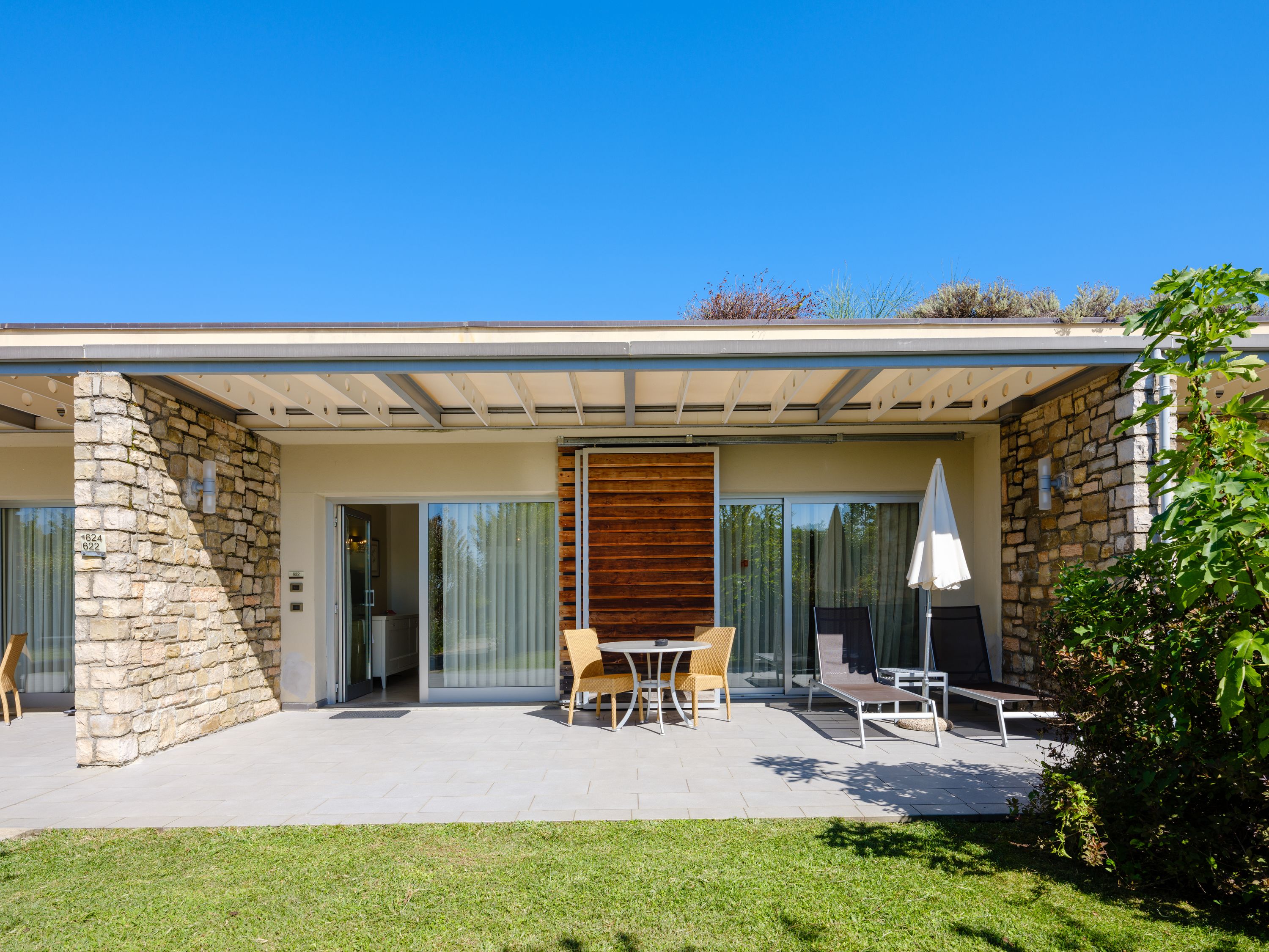 A modern house with a stone exterior, a wooden slatted wall, and a patio with outdoor furniture.