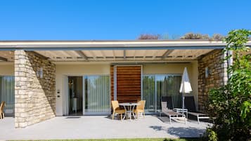 Una casa moderna con fachada de piedra, pared de listones de madera y patio con mobiliario exterior.