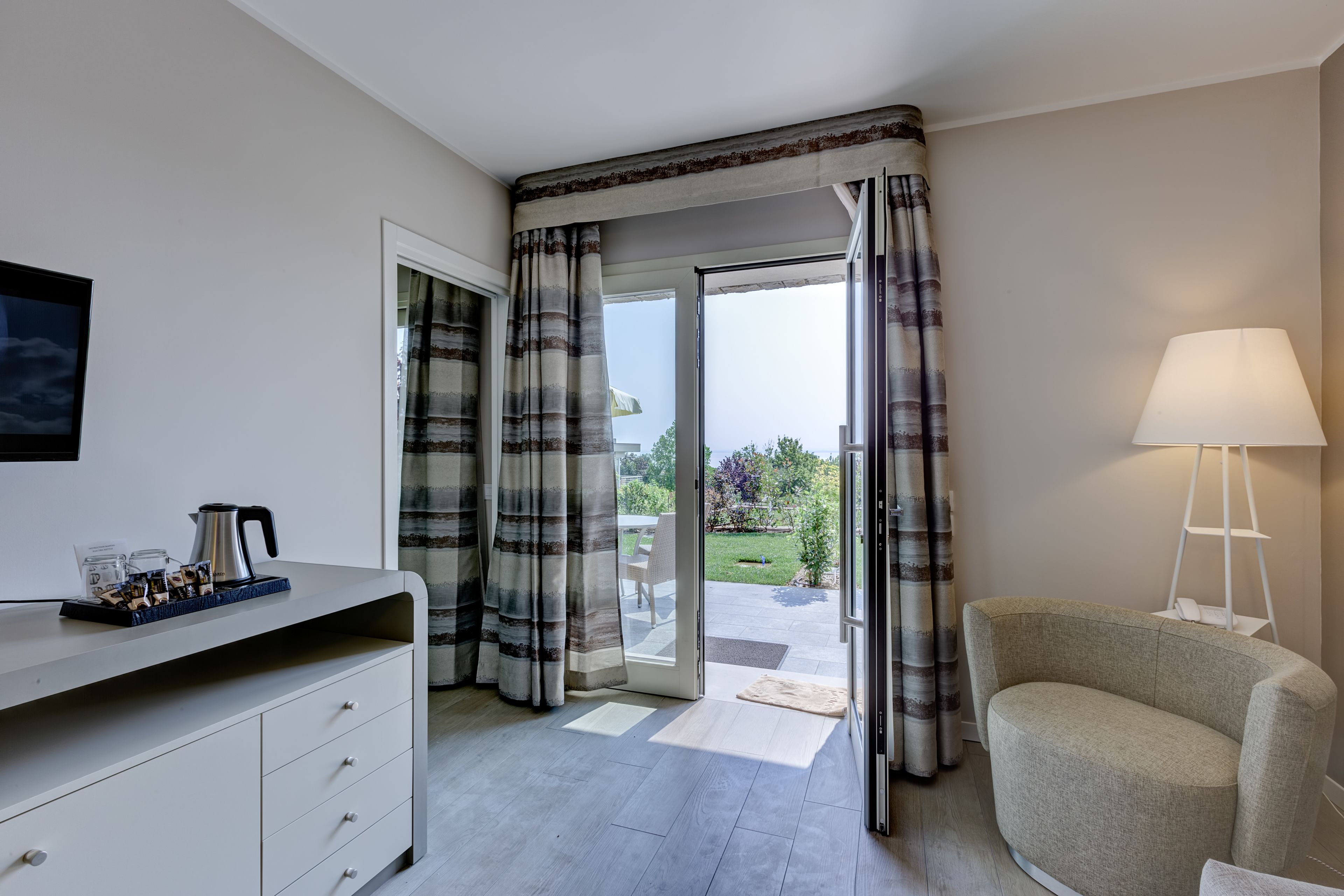 A room with a sofa, a lamp, a coffee table with a kettle, and a view of the outdoors through a glass door.