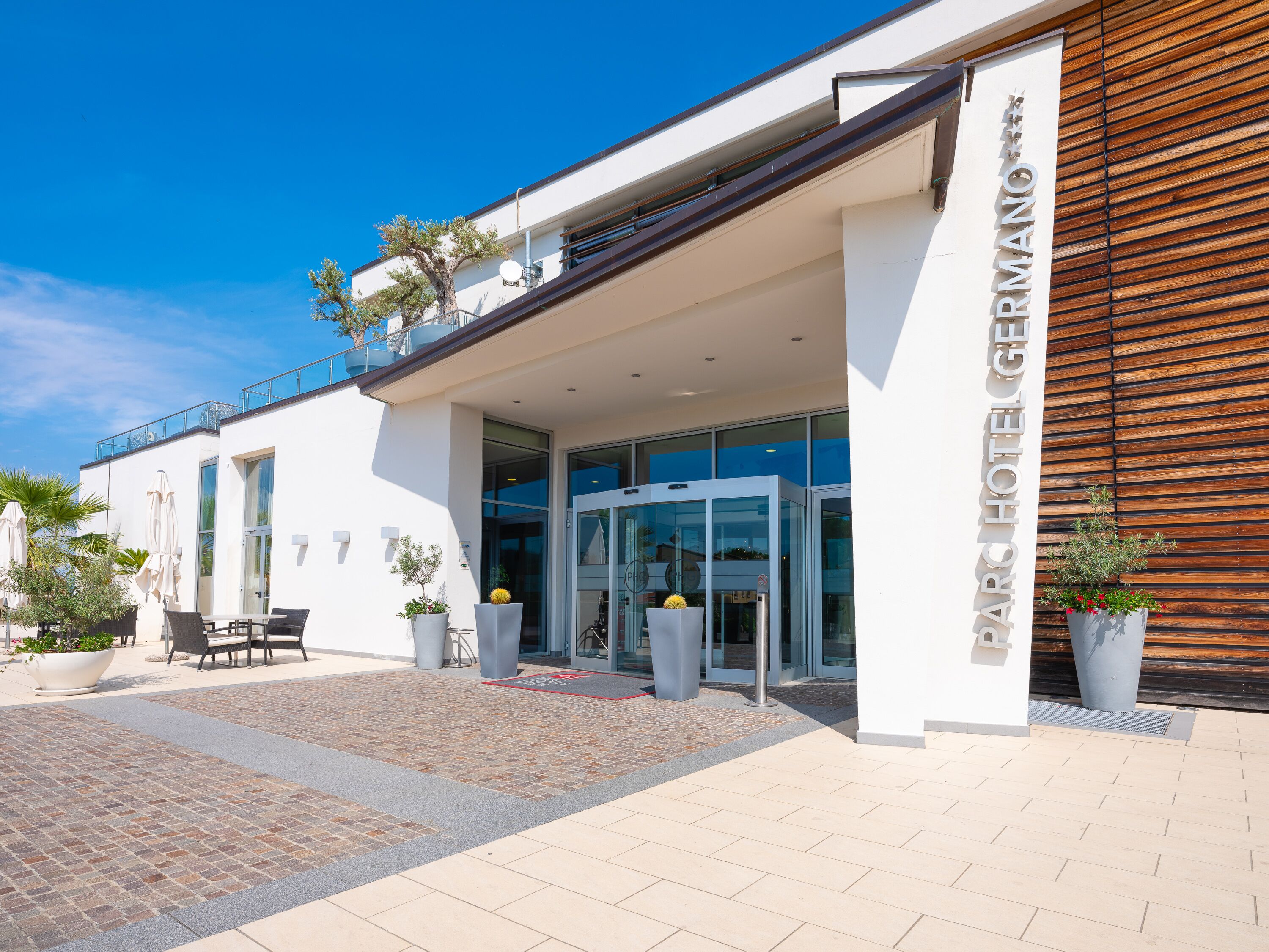 A modern hotel entrance with a revolving door, outdoor seating, and potted plants.