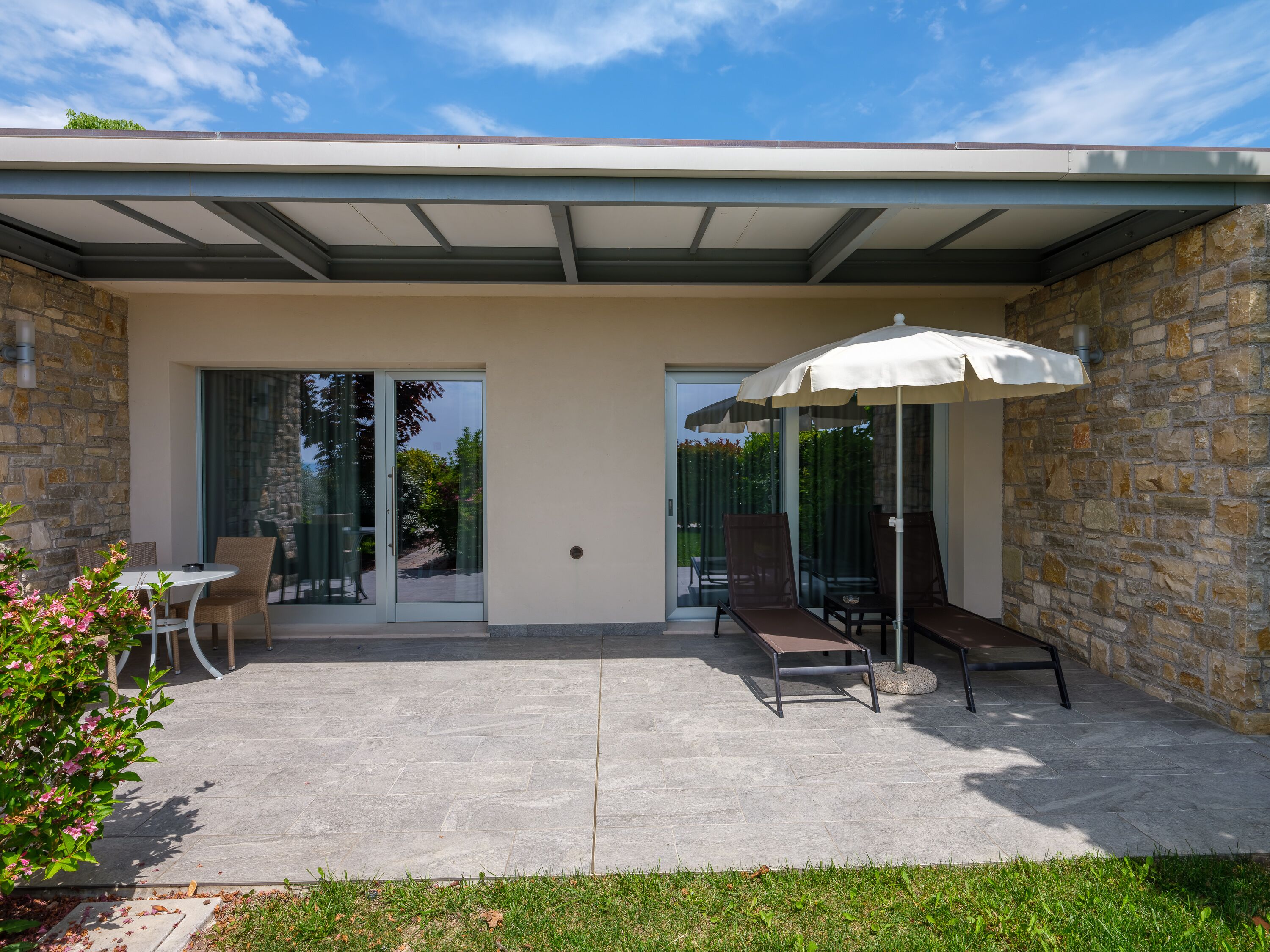 A covered patio with a table and chairs, a lounge chair, and an umbrella.