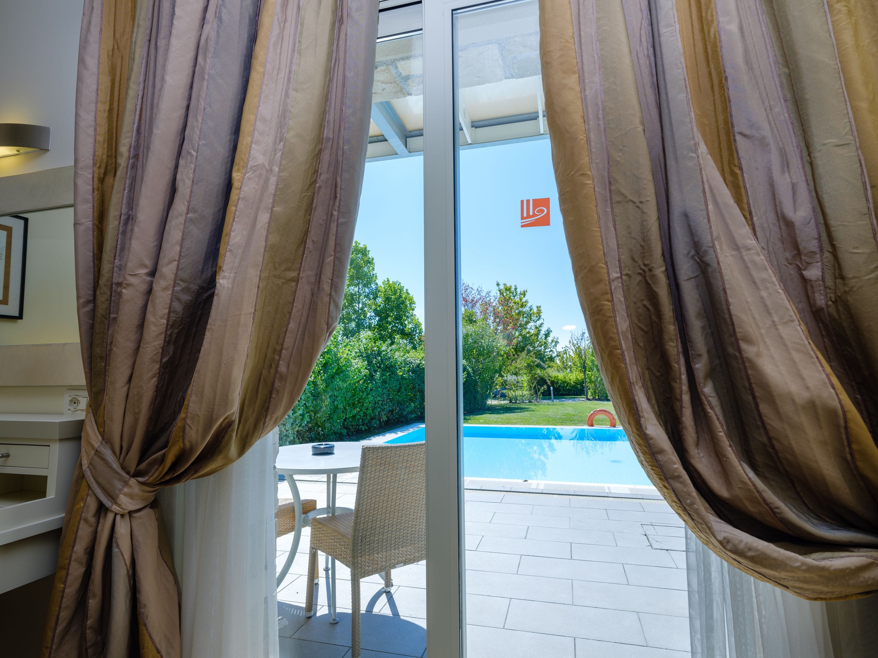 A room with a sliding glass door leading to an outdoor area with a pool and a table with chairs.