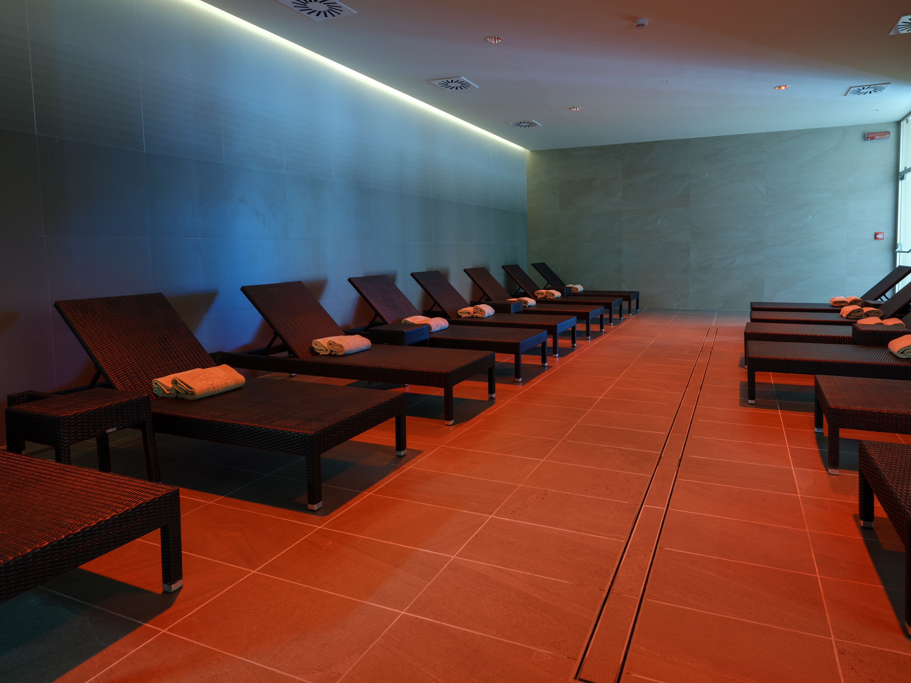 A row of sun loungers with towels, a tiled floor, and a blue wall.