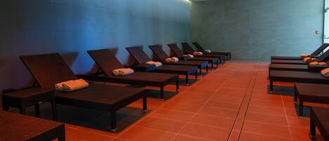 A row of sun loungers with towels, a tiled floor, and a blue wall.