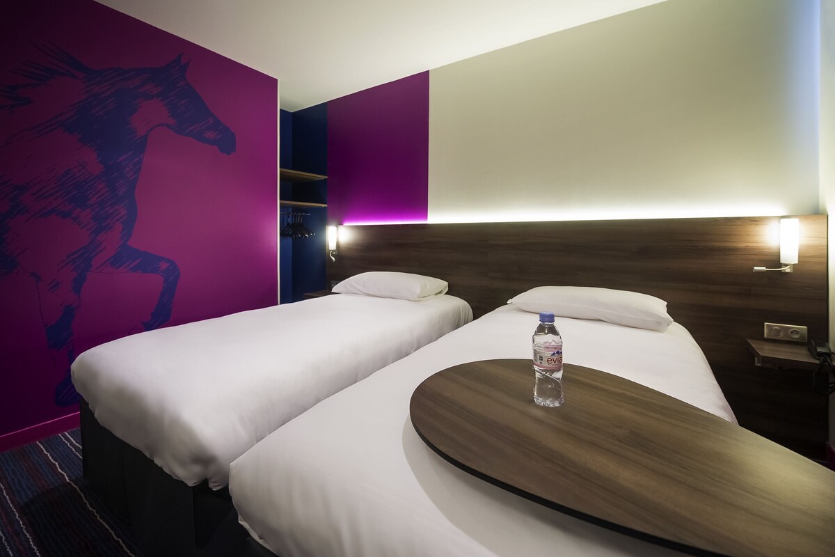 Una habitación de hotel con dos camas individuales, un cabecero de madera, una mesita de noche con una lámpara y una pared decorada con un mural de caballos.