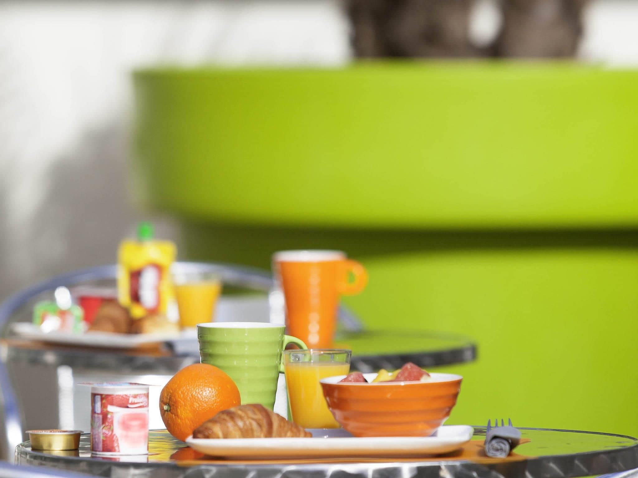 Una mesa de vidrio con un desayuno que incluye un croissant, una naranja y un vaso de zumo de naranja.