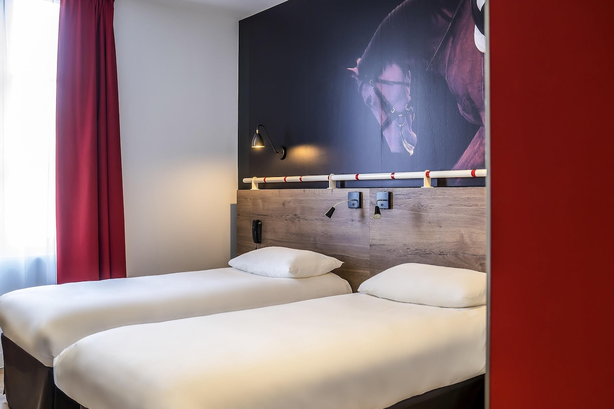 A hotel room with two beds, a wooden headboard, a mounted phone, and a wall-mounted light fixture.