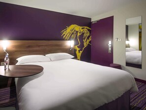 A hotel room with a large bed, a round table with a bottle, a wall-mounted lamp, and a large mirror. - ibis Styles Saumur Gare Centre (Saumur)