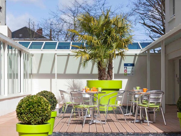 A patio with a table and chairs, a palm tree, and a sign indicating a reception area. - ibis Styles Saumur Gare Centre (Saumur)
