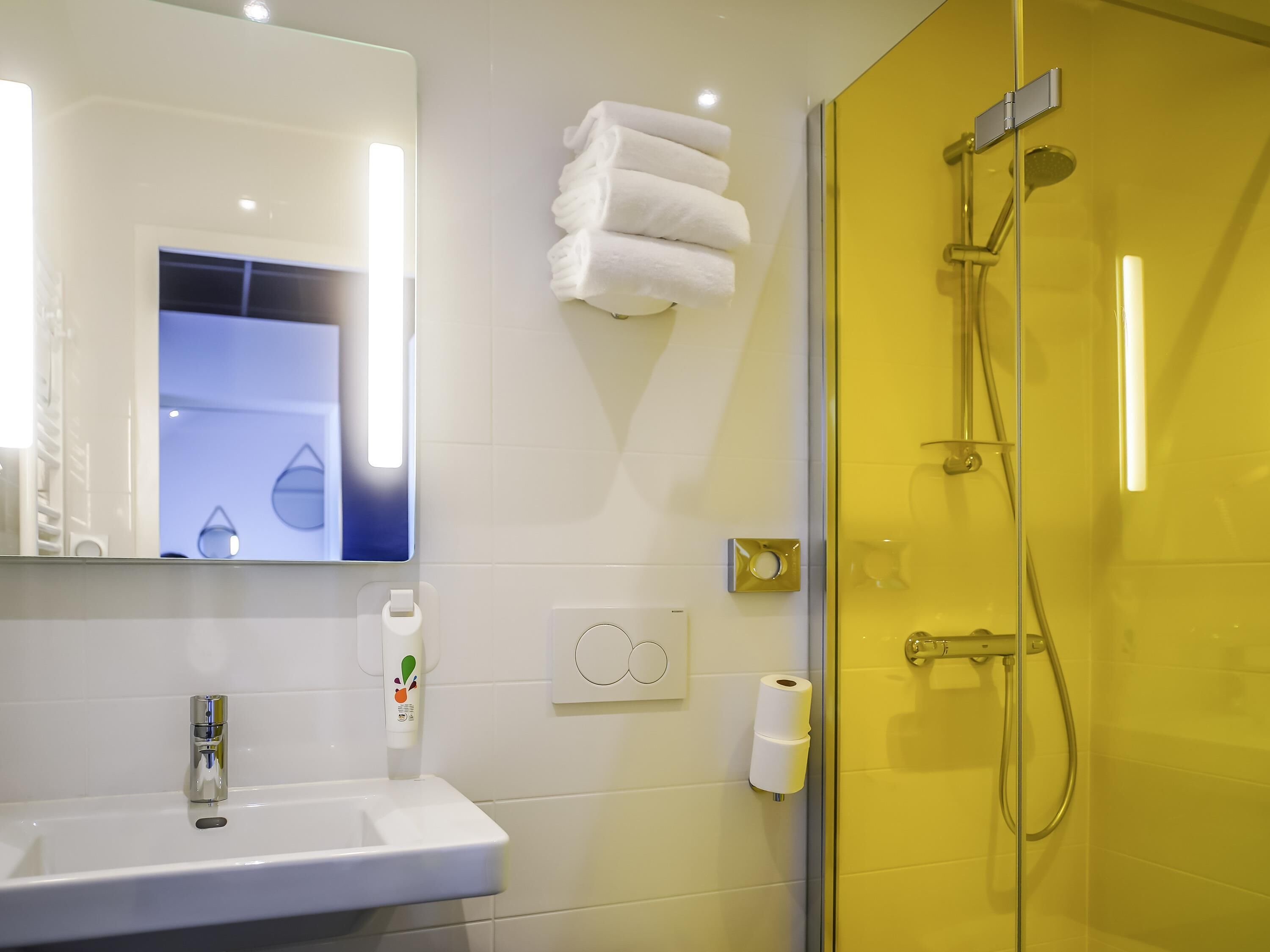 Een badkamer met een witte wastafel, een spiegel, een handdoekhouder, een toiletpapierrolhouder en een douche met een glazen deur.