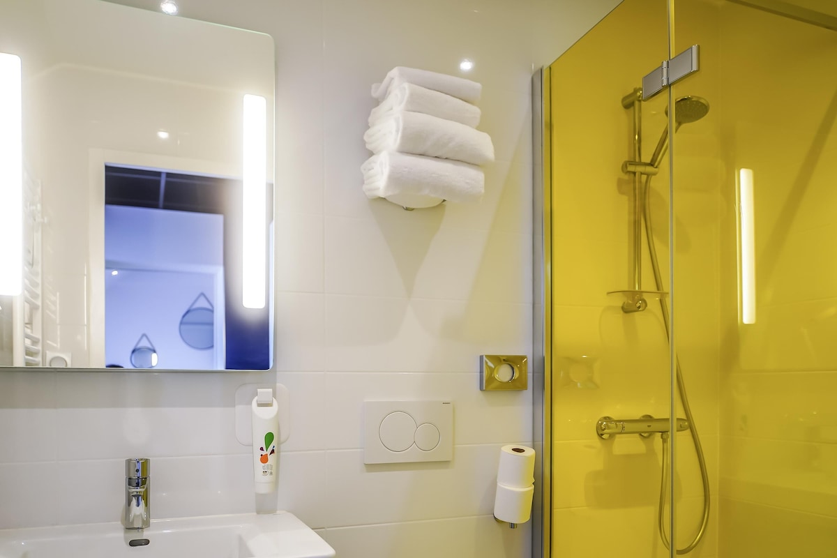 A bathroom with a white sink, a mirror, a towel rack, a toilet paper holder, and a shower with a glass door.