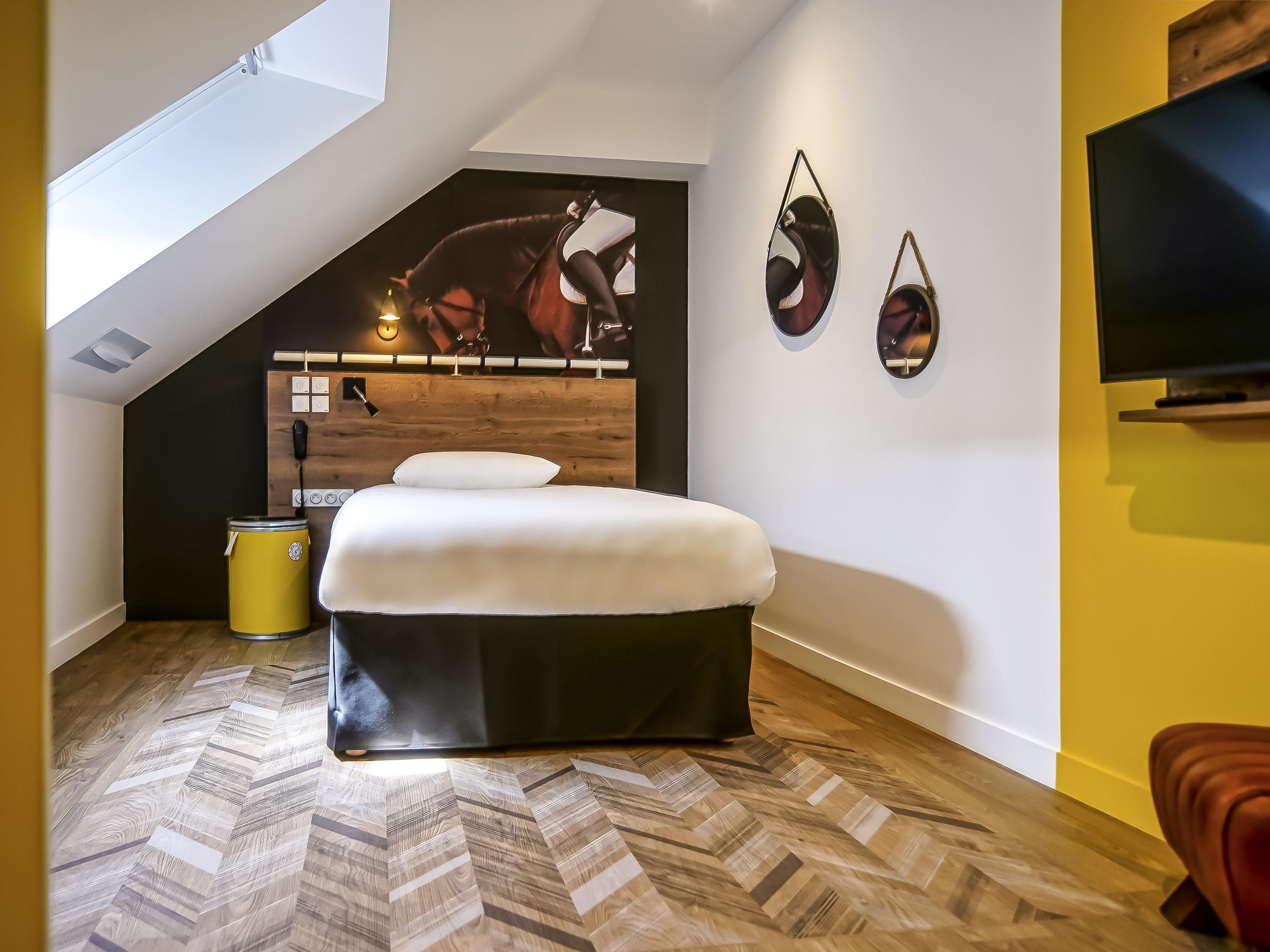 Une chambre à coucher avec un lit, une tête de lit en bois, un téléviseur fixé au mur et un luminaire au plafond.