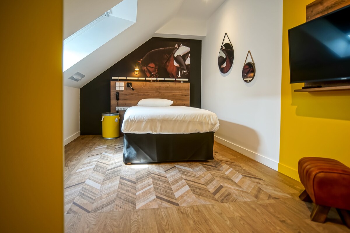Un dormitorio con techo inclinado, una cama con cabecera de madera, un cubo de basura amarillo y un televisor montado en la pared.