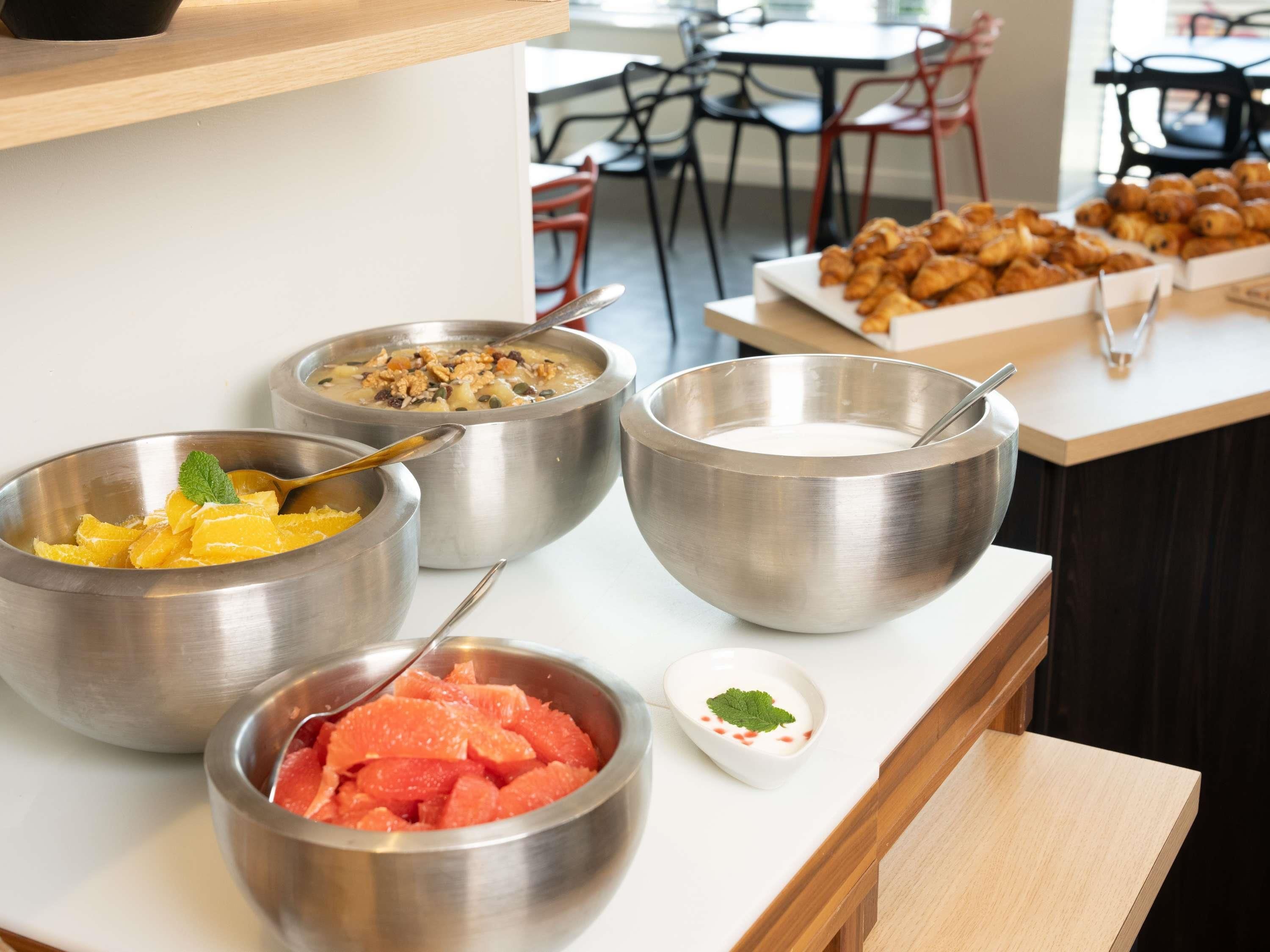 Uma mesa de buffet com diversos alimentos, incluindo potes de fruta, uma tigela de sopa e um prato de doces.