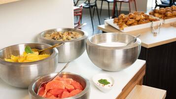 Uma mesa de buffet com diversos alimentos, incluindo potes de fruta, uma tigela de sopa e um prato de doces.