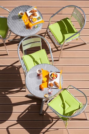 A deck with outdoor furniture, including round tables and chairs with green cushions, and a variety of breakfast items. - ibis Styles Saumur Gare Centre (Saumur)