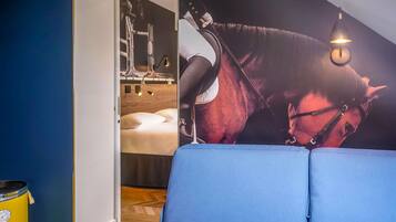 A room with a blue sofa, a wall-mounted light fixture, and a poster of a horse.